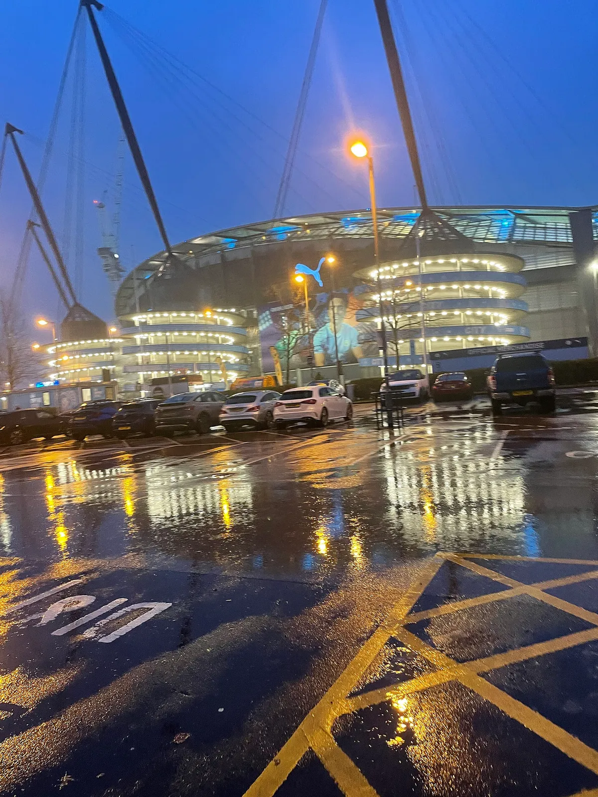 Real night view of Etihad Stadium reflected in the wet approach outside the ground